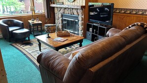 A cozy living room with a stone fireplace, leather sofa, wooden coffee table, and a television.