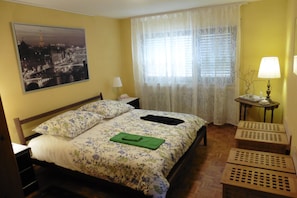 Enjoy a restful stay in this cozy room with a neatly made bed, wooden floor, and a table with a lamp.