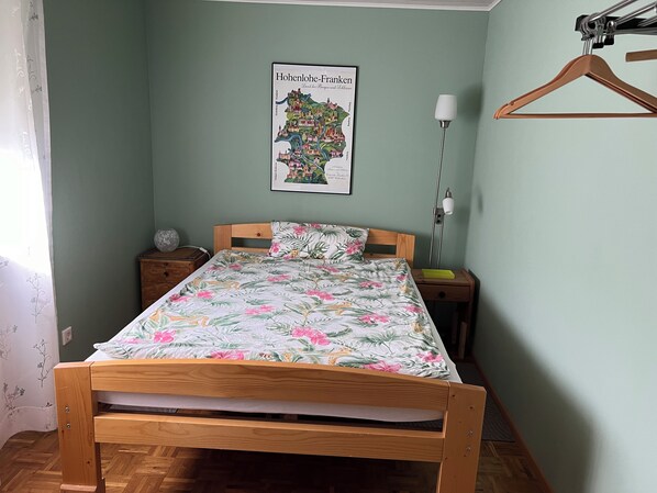 A bedroom with a wooden bed, a nightstand, a lamp, and a map of Hohenlohe-Franken on the wall. - Apartment in Quiet location, family-friendly, with proximity to the Tauber Valley Cycle (Igersheim)