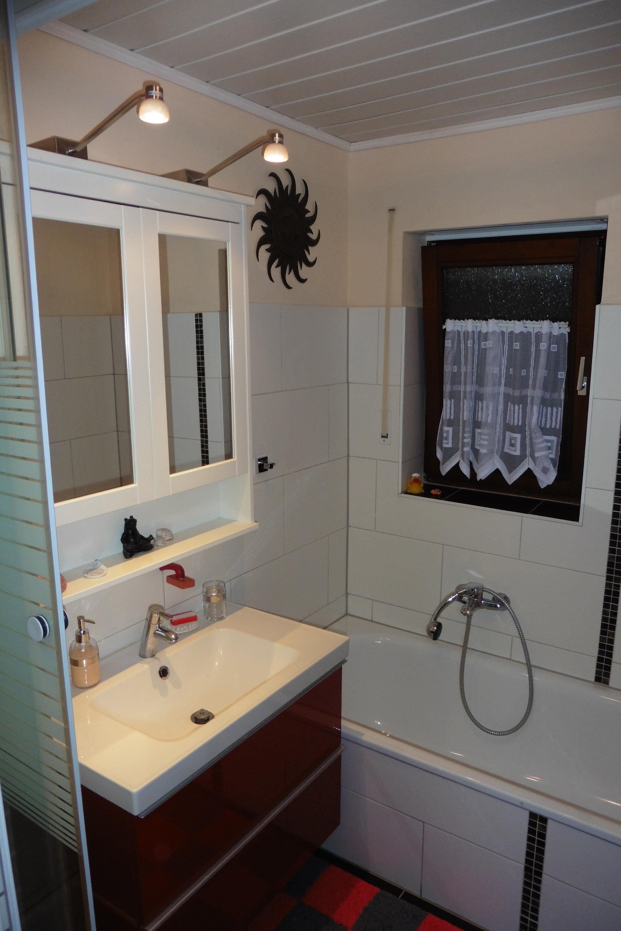 A bathroom with a white sink, a mirror, a bathtub, and a window with a curtain.