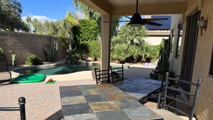 Une terrasse avec une table et des chaises, une piscine et de la verdure tout autour.