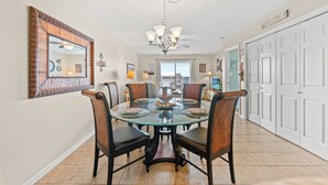A dining area with a glass table, six chairs, a chandelier, and a large mirror on the wall. - Spacious 2 Bedroom/2 bathroom Condo with Ocean View, Pool, Elevator, and Balcony (North Myrtle Beach)