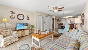 A living room with a sofa, television, and a dining area with chairs and a table. - Spacious 2 Bedroom/2 bathroom Condo with Ocean View, Pool, Elevator, and Balcony (North Myrtle Beach)