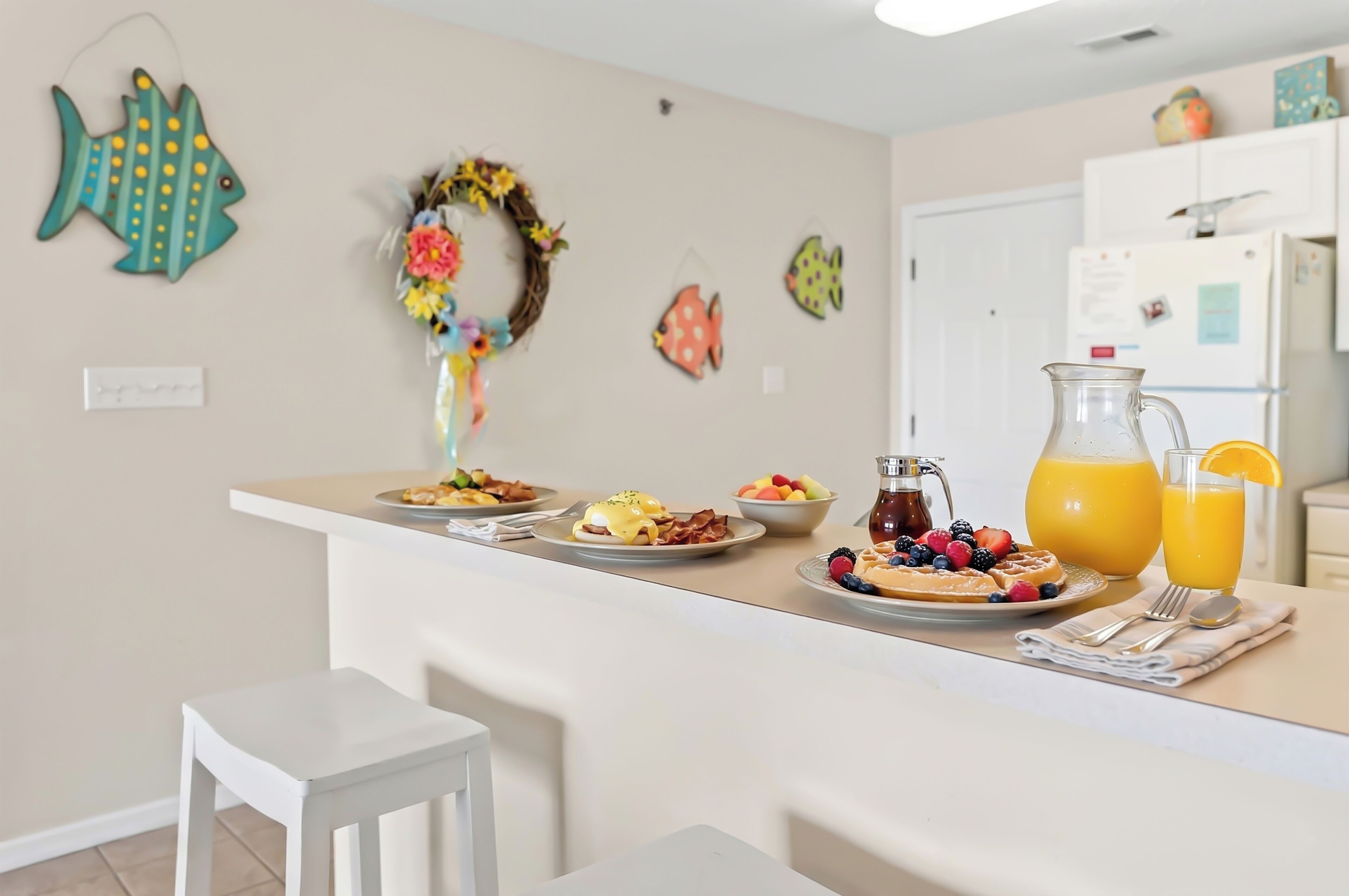 A kitchen counter with breakfast items, a refrigerator, and wall decorations.