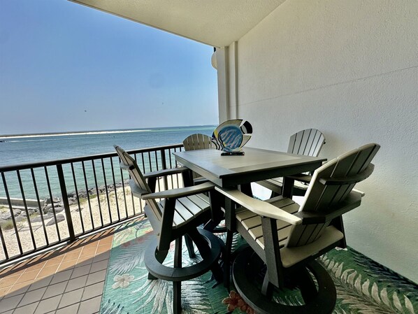 A balcony with a table and chairs, overlooking a beach and the ocean. - Beautiful 2nd Floor Condo located on the Beach with Views of The Pass (Orange Beach)