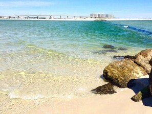 Ein Strand mit klarem Wasser, Felsen und einem Pier im Hintergrund.