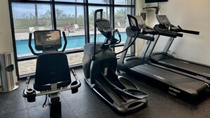 Una palestra con tapis roulant, ellittiche e cyclette, con vista su una zona piscina.