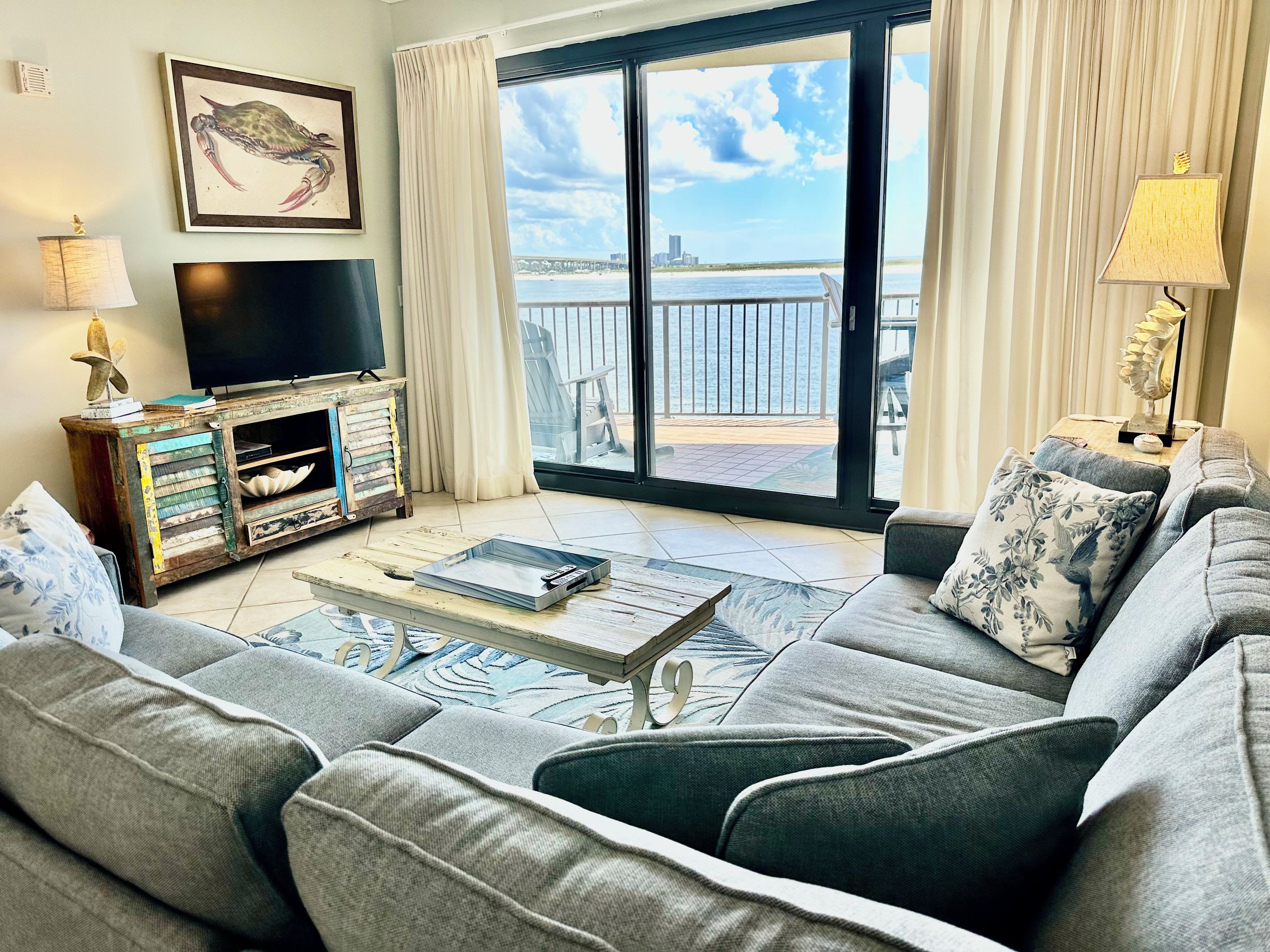 A living room with a sofa, a television, a wooden cabinet, and a view of the sea through a glass door.