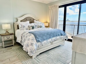 A bedroom with a bed, nightstand, lamp, and a view of the sea.