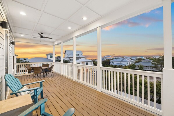 A covered outdoor deck with a view of houses, a ceiling fan, and outdoor furniture.