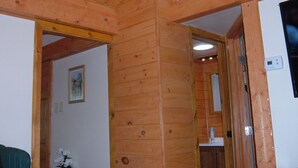 A wooden interior with a visible doorway leading to another room, a light fixture on the ceiling, and a wall-mounted light switch. - CEDAR CREST CABIN NEAR DOUGLAS LAKE. 30 MILES AWAY FROM GATLIN BURG.   (NEWPORT)