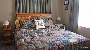 A bedroom with a large bed, two bedside tables, a headboard, and a window with curtains. - Private Retreat in the Rocky Mountain Front with a Million Dollar View  (Choteau)