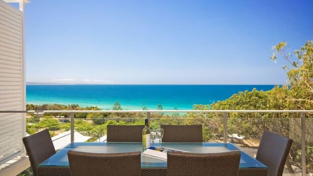 A balcony with a glass table and wicker chairs, overlooking a turquoise sea and a clear sky. - Ocean View 1 - Rainbow Beach. Luxury With Unrivalled Views. Stunning views. (RAINBOW BEACH)