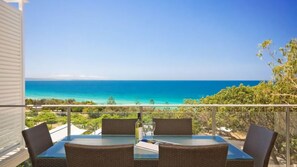 A balcony with a glass table and wicker chairs, overlooking a turquoise sea and a clear sky. - Ocean View 1 - Rainbow Beach. Luxury With Unrivalled Views. Stunning views. (RAINBOW BEACH)