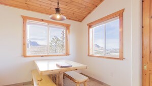 Une pièce avec une table et un banc en bois, de grandes fenêtres offrant une vue sur les montagnes et un plafond en bois.