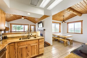 A kitchen with wooden cabinets, a granite countertop, a sink, and a dining area with a wooden table and benches.