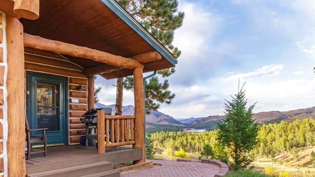 Une cabane en rondins avec un porche, un barbecue et une vue sur une vallée boisée.