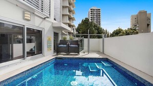 A modern building with a swimming pool, outdoor seating, and a view of surrounding high-rise buildings. - Rainbow Bay Villa - Spacious and Luxurious (Coolangatta)