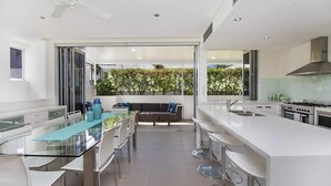 A modern kitchen with a central island, bar stools, and a dining area with a glass table. - Rainbow Bay Villa - Spacious and Luxurious (Coolangatta)