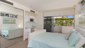 Une chambre à coucher avec un lit, un bureau et un balcon donnant sur la verdure.