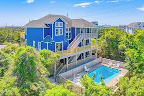A multi-story house with a pool, surrounded by trees.