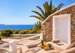 A stone building with a white door, a balcony with a white railing, and a view of the sea.
