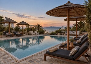 A poolside area with lounge chairs, umbrellas, and a view of the sea.