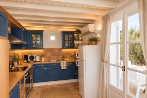 A kitchen with blue cabinets, a white refrigerator, and a window with curtains.