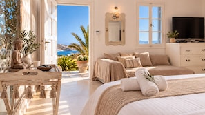 A bedroom with a bed, a television, a bedside table, and a view of the sea.