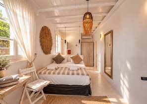 A bedroom with a bed, bedside tables, a mirror, and a hanging light fixture.