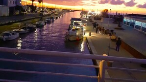 A waterfront marina with boats docked along the shore, a pedestrian walkway, and a bridge in the background. - Cozy stone house in the green, sea-lake view, garden, air cond. WIFI, washer (Montigiano)