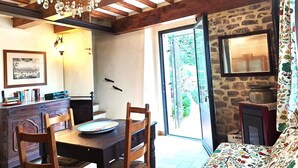 A dining area with a wooden table, chairs, and a chandelier. There is a stone wall and a door leading outside. - Cozy stone house in the green, sea-lake view, garden, air cond. WIFI, washer (Montigiano)