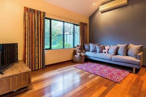 A living room with a sofa, a television, a colorful rug, and a window with curtains.