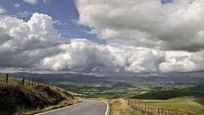 Un camino serpenteante a través de un paisaje montañoso, con una cerca a un lado y un cielo despejado.