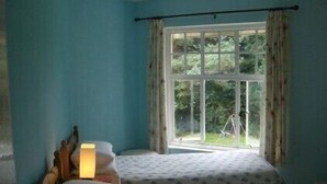 Una habitación con dos camas, una ventana con cortinas y una lámpara a la izquierda.