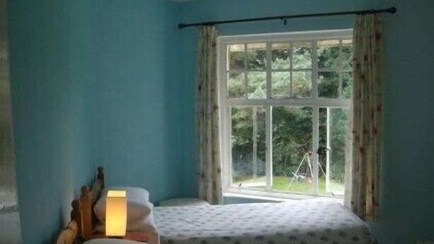 A room with two beds, a window with curtains, and a lamp on the left side.