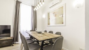 Ein modernes Wohnzimmer mit einem Holzesstisch, grau gepolsterten Sesseln, einem Flachbildfernseher und einem großen abstrakten Gemälde an der Wand.