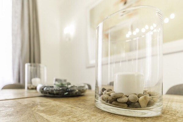 A clear glass container with a white candle and pebbles on a wooden surface.