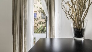 Ein freier Blick auf ein Fenster mit Vorhängen, eine Glasvase mit Zweigen und eine Zeitschrift auf einem Tisch.