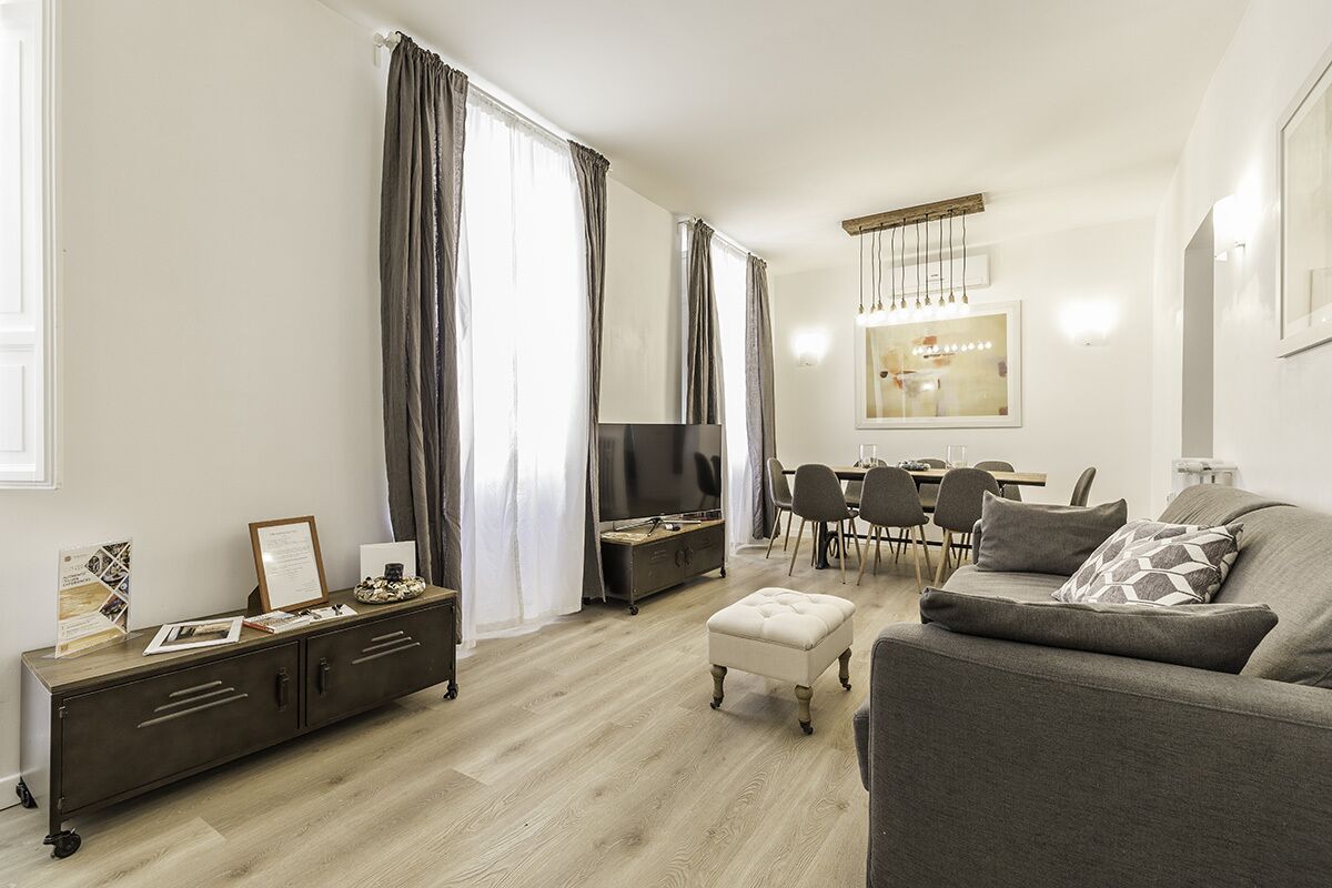 A modern living room with a grey sofa, a wooden cabinet, a TV, and a dining area with chairs and a table.