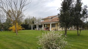 Ein Haus mit überdachter Terrasse, Rasen und Garten mit blühenden Pflanzen.