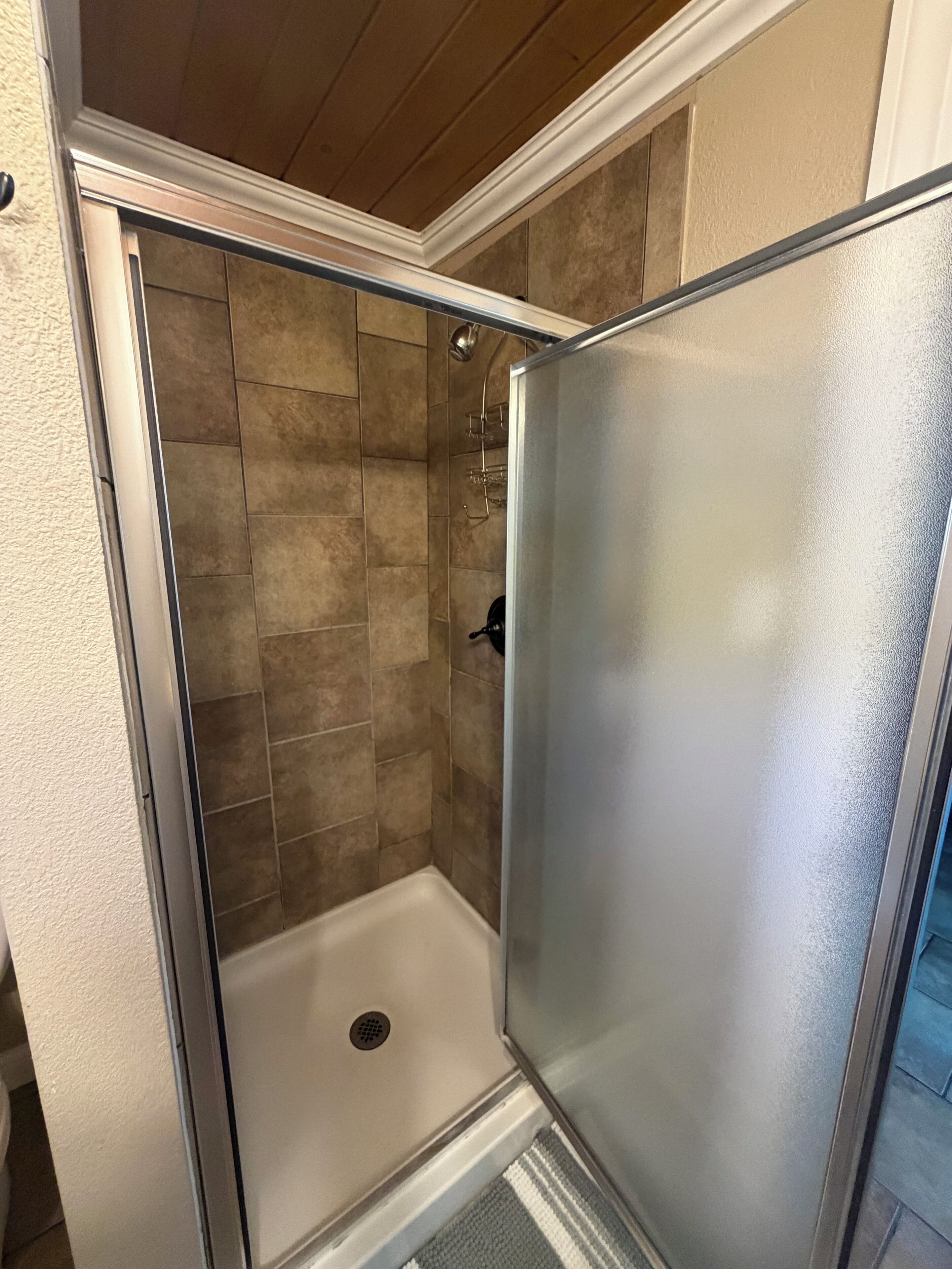 Une douche avec une porte en verre, des murs carrelés et un plafond en bois.