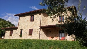 A stone building with a flat roof, multiple windows, and a small porch area with outdoor seating. - Ancient Plan. Appart in the Greenest Umbria: Nature, History, Genuineness, Relax (Nocera Umbra (PG))