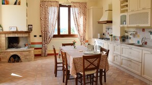 A dining area with a table set for four, a fireplace, and a kitchen with white cabinets and a tiled backsplash. - Ancient Plan. Appart in the Greenest Umbria: Nature, History, Genuineness, Relax (Nocera Umbra (PG))