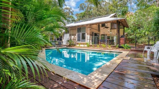 A poolside area with a swimming pool, wooden deck, and a house with a covered patio. - 7 Naiad Court - Rainbow Shores. Swimming Pool and Walk To Beach. Aircon. Wi-Fi. (RAINBOW BEACH)