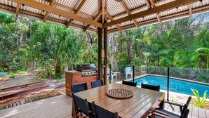 An outdoor patio with a wooden table and chairs, a barbecue grill, and a pool. - 7 Naiad Court - Rainbow Shores. Swimming Pool and Walk To Beach. Aircon. Wi-Fi. (RAINBOW BEACH)