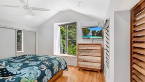 A bedroom with a bed, a wooden dresser, a TV, and a window with a view of greenery. - 7 Naiad Court - Rainbow Shores. Swimming Pool and Walk To Beach. Aircon. Wi-Fi. (RAINBOW BEACH)