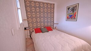 A bedroom with a bed, a patterned headboard, a poster on the wall, and a window. - Apartment for 4 people – Sea view – Air conditioning – Downtown – Sainte Maxime (STE MAXIME)