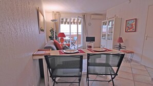 A dining area with a table set for two, a sofa, a TV, and a balcony with a view. - Apartment for 4 people – Sea view – Air conditioning – Downtown – Sainte Maxime (STE MAXIME)