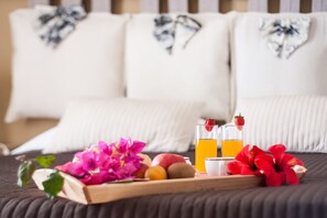 En säng med vita kuddar och ett träbricka med frukt, blommor och ett glas apelsinjuice.